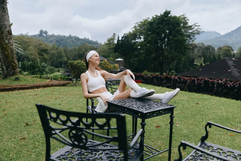 Young woman in active wear enjoying a peaceful moment in a lush garden, promoting healthy lifestyle and fitness