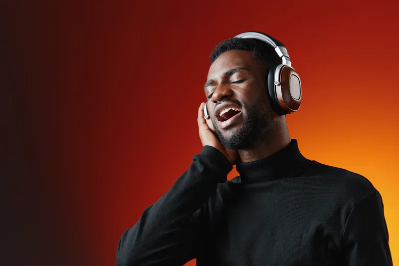 Joyful Black man singing passionately while wearing headphones against a vibrant orange background, showcasing emotion and joy in music appreciation