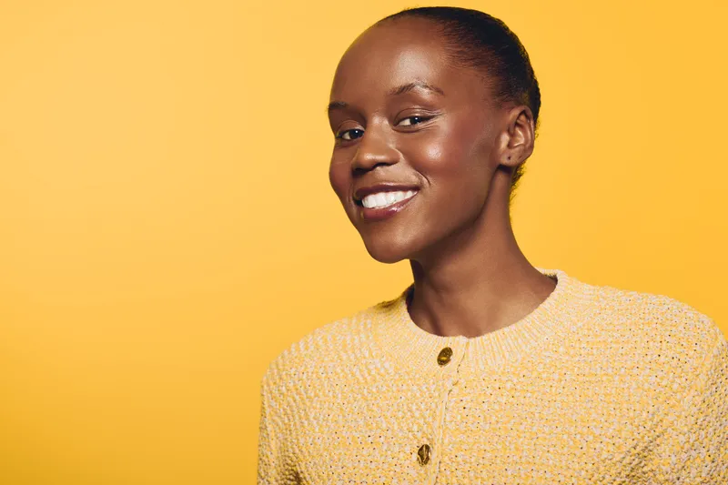 Portrait of a smiling African woman with dark skin wearing a yellow sweater against a yellow background. Concept of happiness, beauty, and confident young adult female.
