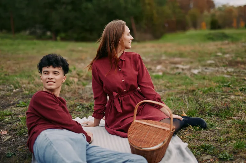 A young couple sharing an authentic outdoor picnic scene, relaxed on a blanket in casual clothing with natural expressions, conveying genuine connection and quiet companionship, emphasizing