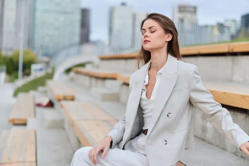 Confident businesswoman in a light gray suit sitting outdoors, showcasing serenity and professionalism in an urban environment.