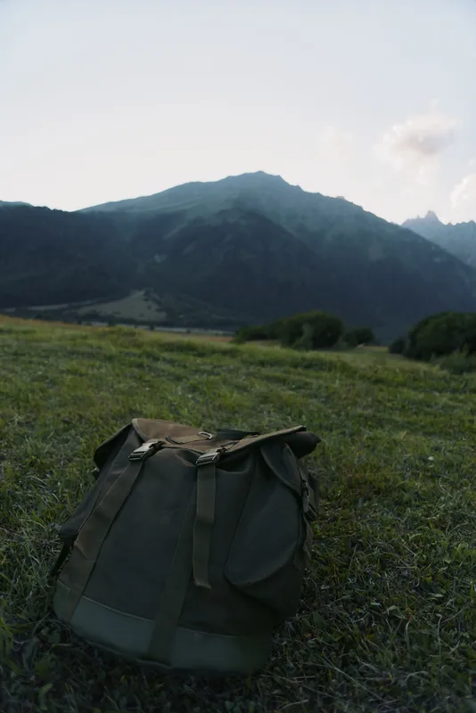Outdoor travel scene featuring a backpack on a grassy meadow with distant mountains under a clear sky, conveying adventure, nature, and solitary exploration for hikers and dreamers!