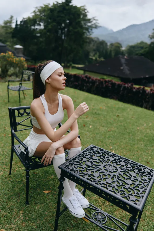 Young athletic woman in sportswear sitting outdoors, expressing calmness and focus amidst a lush green landscape, perfect for promoting active lifestyle and fitness