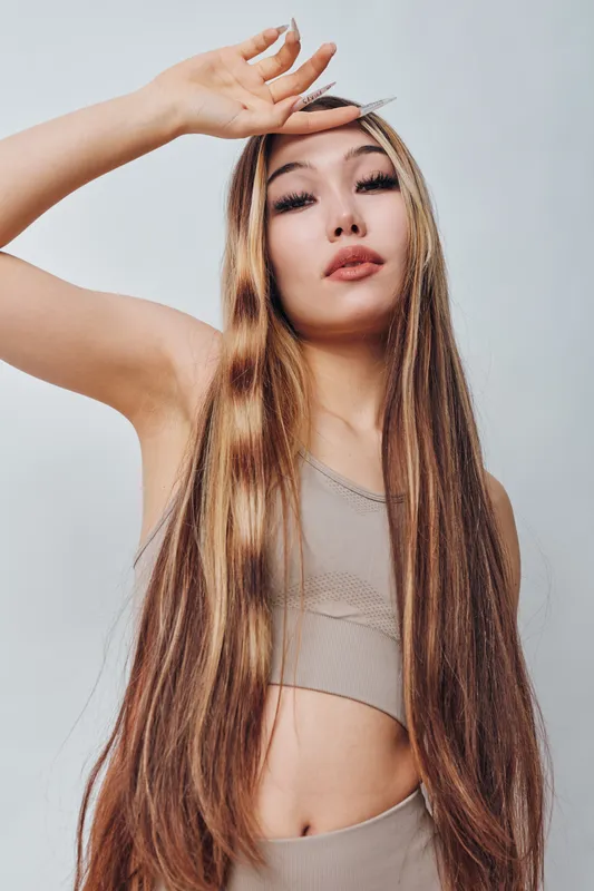 Woman with long highlighted hair and natural makeup posing with hand over forehead. Beauty, fashion and confident female model in casual neutral clothing on light background.