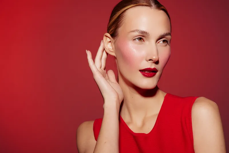 Portrait of a woman with red lipstick and blush wearing a red sleeveless top on red background. Concept of beauty, fashion, makeup, and elegance with soft lighting and confident expression.