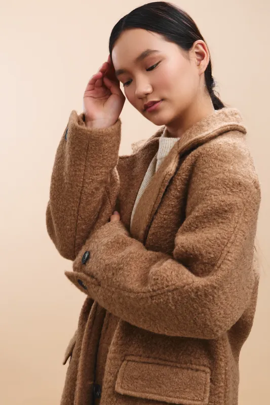 Asian woman wearing a cozy brown coat stands against a soft beige backdrop, exuding calm confidence and a thoughtful pose, perfect for lifestyle, fashion, or commercial projects.
