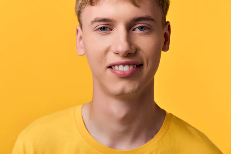 Smiling young man in a bright yellow shirt against a vivid yellow backdrop, closeup studio shot suitable for lifestyle, warmth and youthful branding