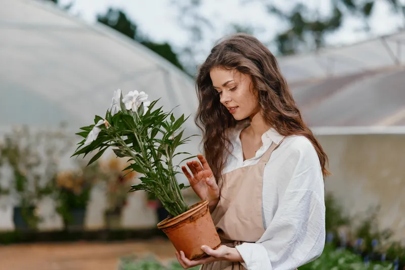 Young woman in natural setting, lovingly caring for potted plant, embodying eco friendly lifestyle, happiness, and connection with nature during springtime
