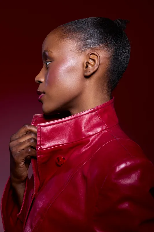 Profile portrait of a black African woman with dark skin wearing a red leather jacket against a dark red background. Concept of fashion, style, confidence, and beauty.
