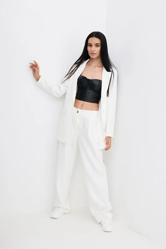 young woman in white suit with black corset top posing against white wall, stylish fashion outfit, minimalistic background, casual elegance, modern look