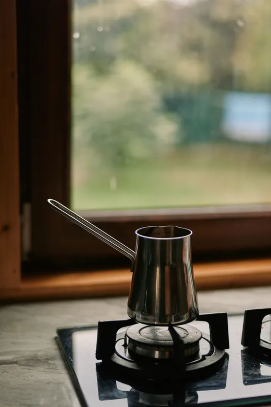 stove gas burner kettle spoon kitchen window metal cookware cooking, warm scene of everyday meal preparation by a bright window, cozy domestic ambiance