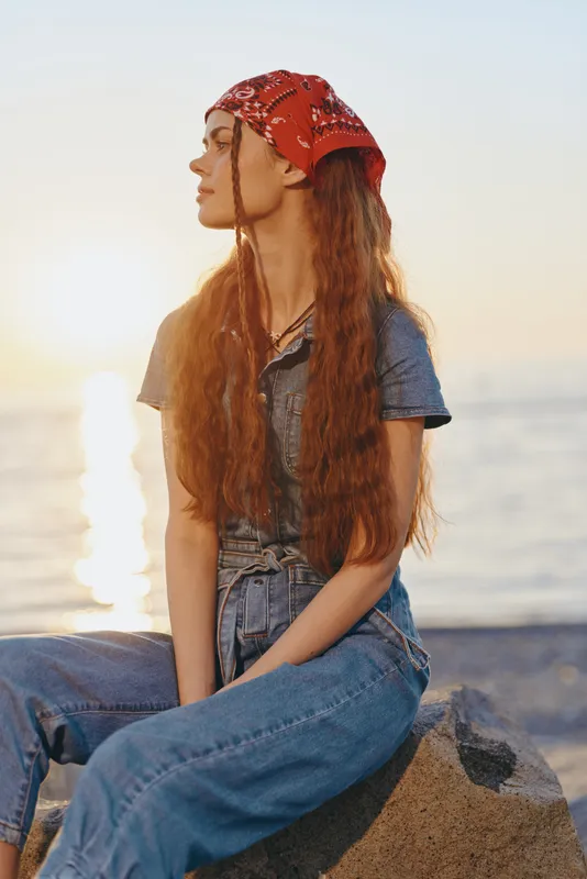 lifestyle woman in modern boho-western denim street style wearing red bandana, casual relaxed pose at sunset with film color warm tones and soft natural light