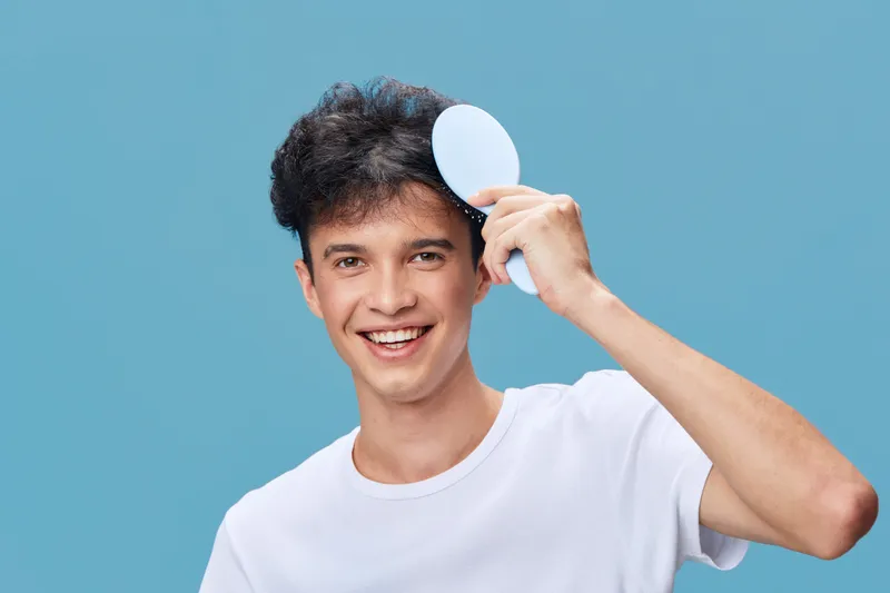 smiling man holding round mirror with white background, casual clothing, friendly expression, isolated on blue, cheerful and youthful mood
