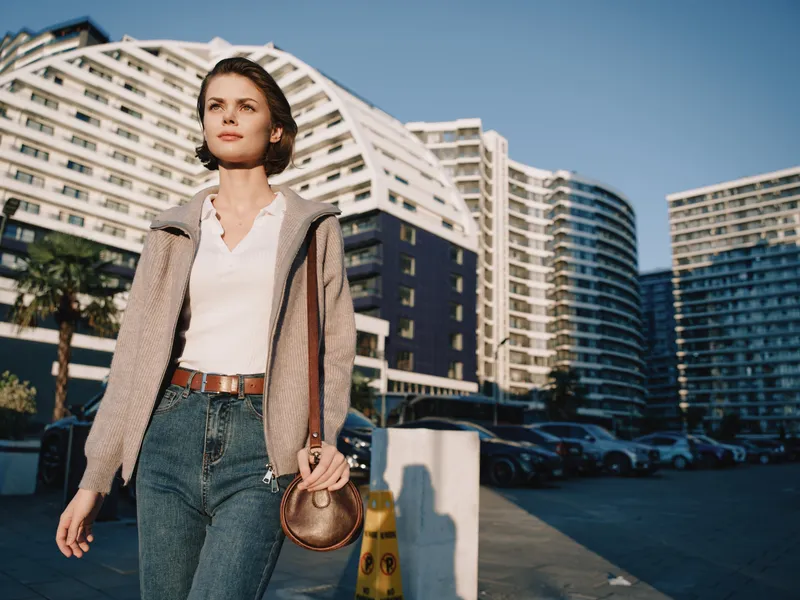 A confident woman walks outdoors past modern high rise buildings, dressed in casual business attire, exuding independence and focus as she heads toward success.