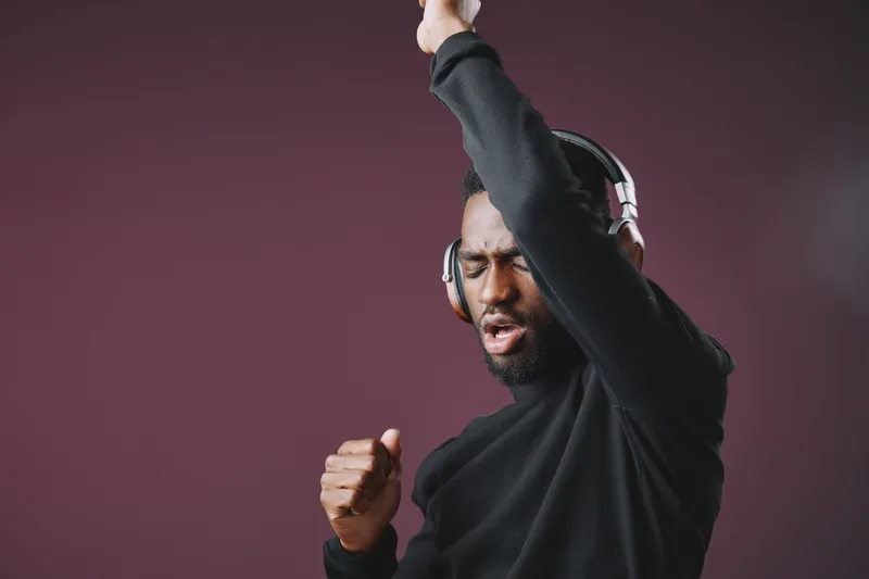 A joyful African man in headphones dancing energetically against a deep purple background, showcasing emotions of happiness and enthusiasm through music