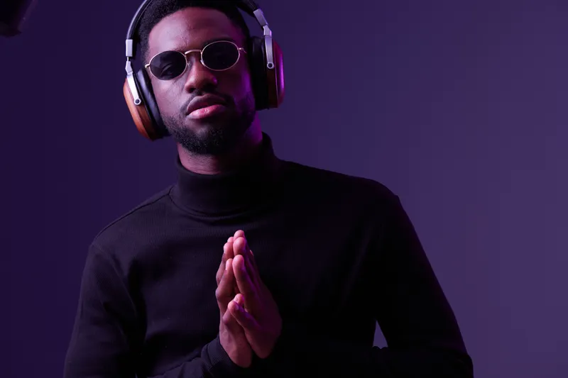 Confident young man wearing headphones and sunglasses, posing against a vibrant purple background showcasing urban lifestyle, music and modern fashion