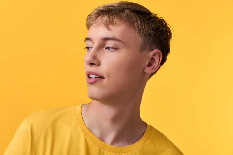 Man in a bright yellow shirt against a matching studio background, relaxed pose and subtle smile, fashion oriented mood with warm lighting and minimal clutter for lifestyle and product use