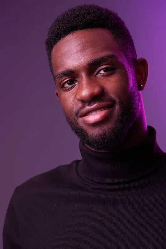Portrait of a smiling African American man in a black turtleneck against a purple background, conveying confidence and style, ideal for fashion and lifestyle themes