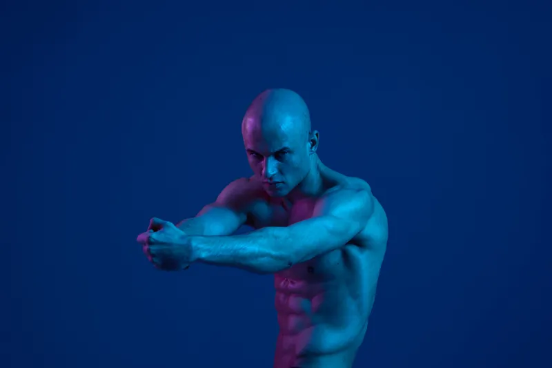 Strong man posing against a blue background, showcasing athletic physique with bold lighting effects. The image captures a sense of empowerment and confidence.