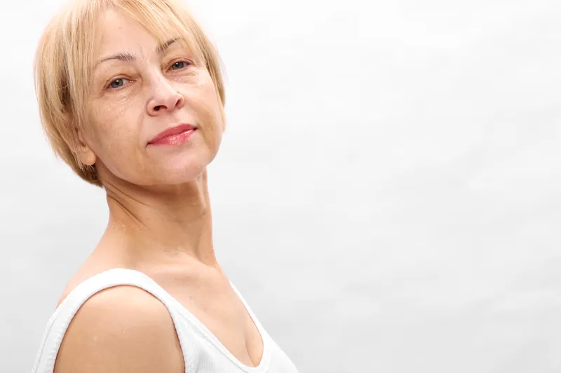 Senior woman portrait closeup smiling gently, beauty and calm mood, studio lighting on soft light background, mature age concept for wellness, health, self confidence