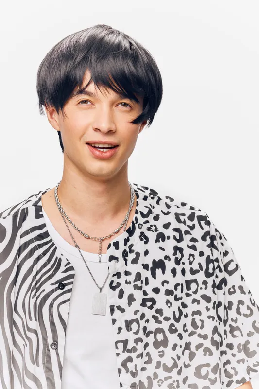 young man with mixed print shirt smiling and looking away, wearing silver chains, short black hair, studio portrait with white background