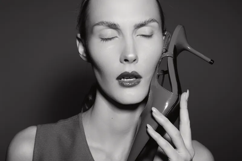 Closeup of a fair skinned European woman with closed eyes holding high heel shoe near face in studio.