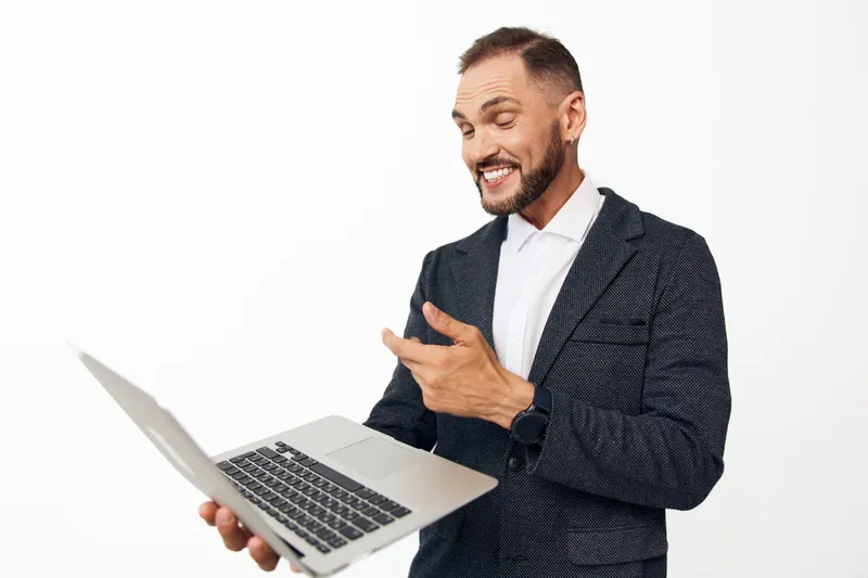 A confident business professional man on an isolated colored background, expressing enthusiasm and energy while presenting ideas with a laptop and clear focus on success.
