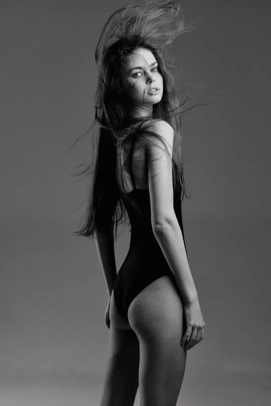 Black and white portrait of a young woman with long hair wearing a bodysuit, posing in a stylish and elegant fashion concept.
