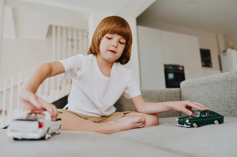 Young boy playing with toy cars indoors, showcasing focus and imagination in a bright, cheerful living room setting.