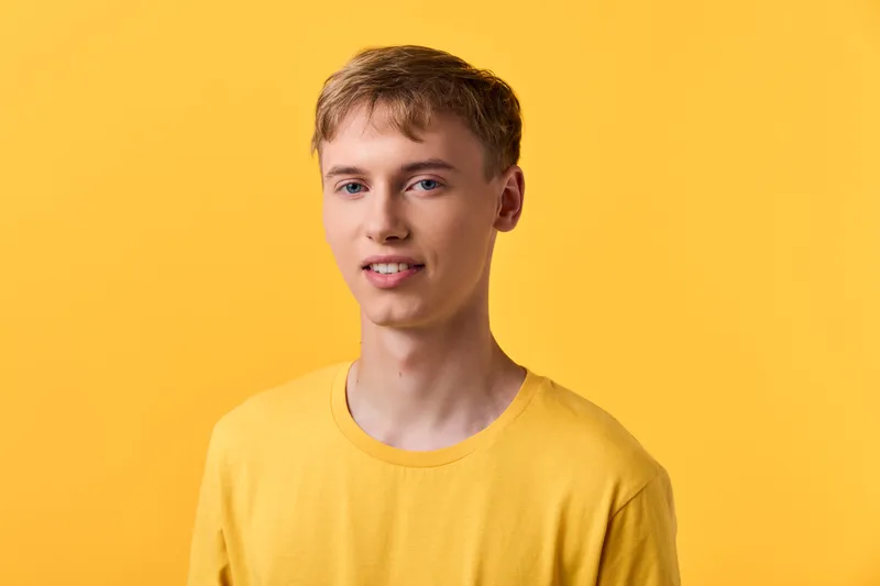 Young man in a yellow t shirt stands against a bright yellow studio background, showcasing casual style, friendly demeanor, and contemporary lifestyle fashion for visual content