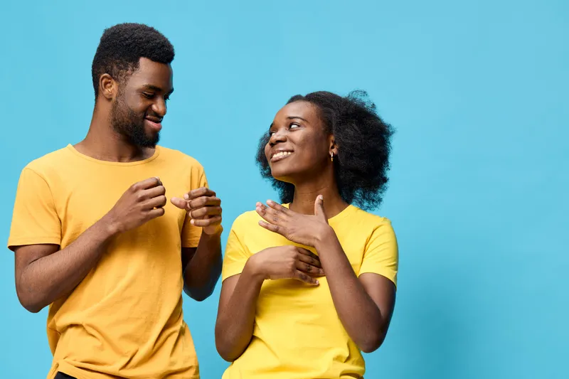 Happy young couple in matching yellow shirts, smiling and interacting playfully against a vibrant blue background, conveying joy and connection