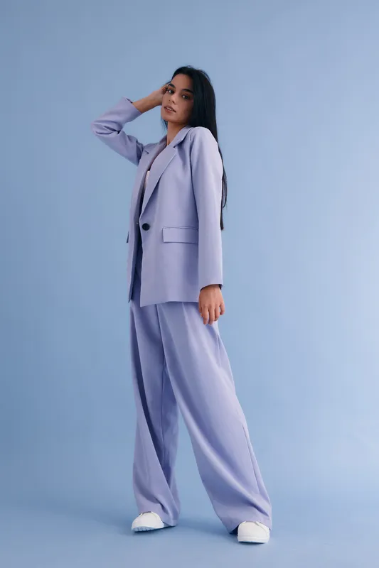 woman in lilac suit posing confidently against blue background, wearing stylish wide trousers and white sneakers, modern fashion concept, full body portrait