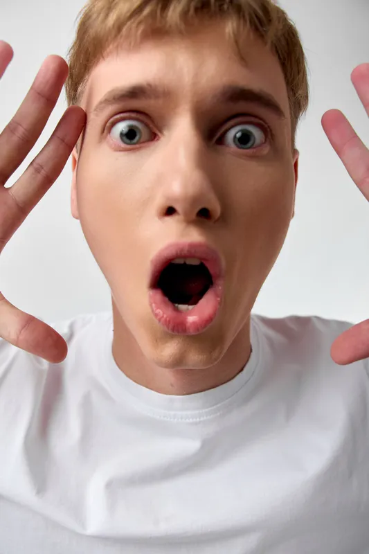 Close up of a surprised man with wide eyes and open mouth, hands raised in shock, conveying astonishment and excitement, strong facial expression for energetic stock imagery and playful consumer