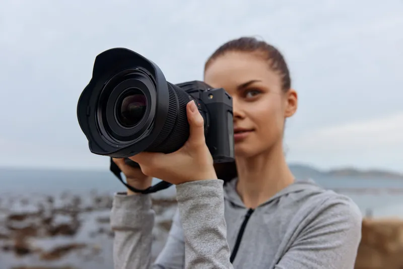 Young woman with a camera on the beach capturing beautiful moments, showcasing passion for photography and nature under a cloudy sky