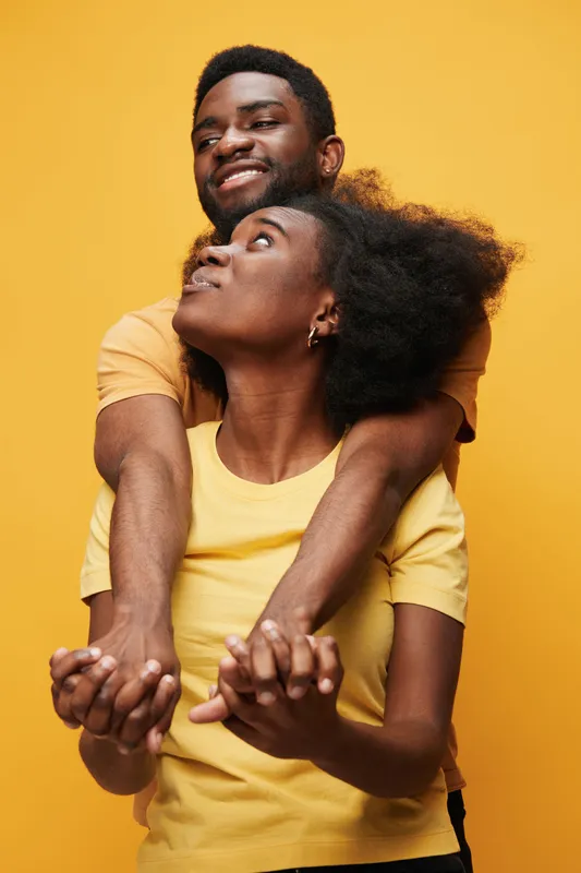 A joyful couple of Black descent embracing against a vibrant yellow background, showcasing love and connection with playful expressions and colorful attire