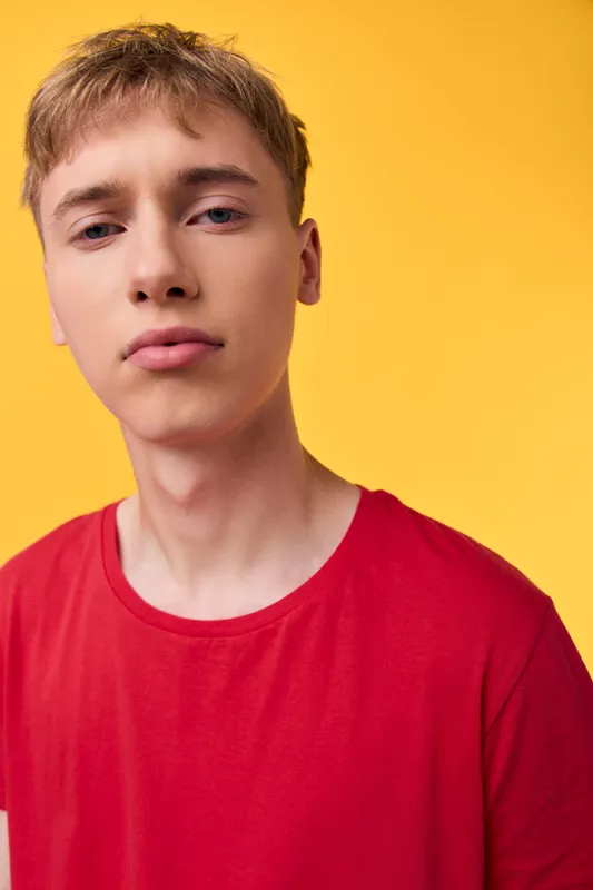 Close up of a young man in a bright red shirt against a vivid yellow backdrop, capturing a relaxed mood and confident gaze, suitable for fashion, lifestyle, or studio shot style without identity