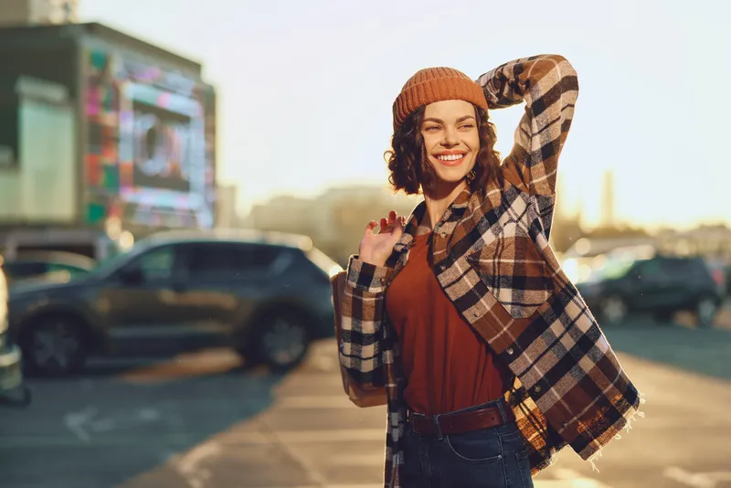Woman smile portrait in urban street at golden hour glow, candid lifestyle capture with authenticity and joyful expression, beanie and plaid coat, mindful living and emotional storytelling vibe.
