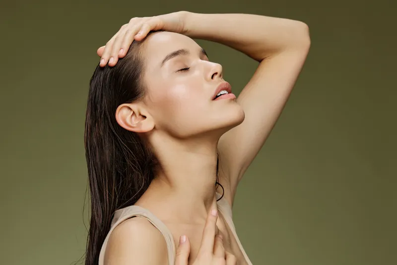 Serene woman with wet hair, gentle expression, posing against a soft green background, embodying beauty and tranquility in fashion photography
