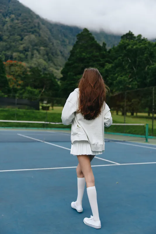 Young woman playing tennis in a sporty outfit on a court, surrounded by lush greenery, conveying a sense of energy and vitality in a sunny outdoor setting