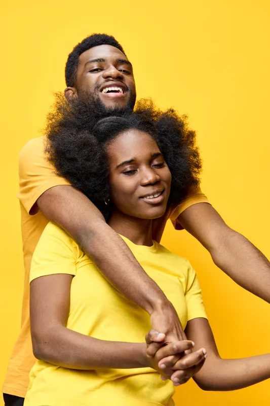 Happy couple with natural hair expressing love in matching yellow shirts, set against a bright yellow background, ideal for relationship and positivity themes