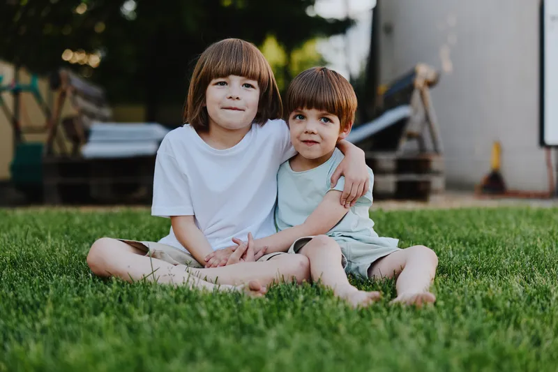 Two smiling children sitting together on the grass, enjoying a sunny day, showcasing friendship and joy in a vibrant outdoor setting.