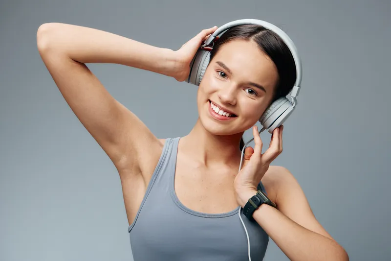 Female athlete in athletic wear, smiling during a workout with headphones in a studio, portrait style, energetic fitness moment and casual gear.
