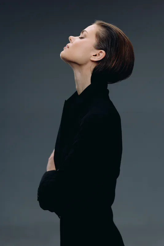 Profile of a thoughtful woman in black clothing with closed eyes, minimalist style and dark background, calm and elegant atmosphere.