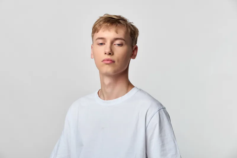Young man with a calm, neutral pose in a white tee, simple studio background, minimal style, clean aesthetic, relaxed vibe, ready for lifestyle use