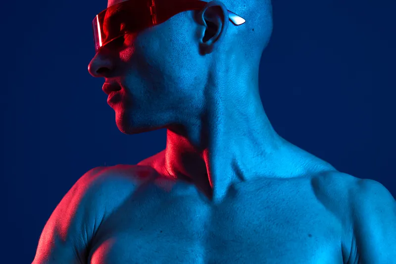 Portrait of a man in vibrant blue and red lighting, showcasing his strong profile and modern accessories for a striking, artistic appearance.