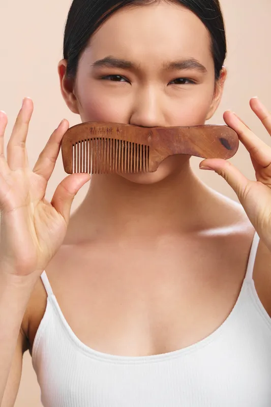 asian woman holds a wooden comb near her lips in a soft portrait, creating a playful and candid moment that highlights natural beauty and relaxed style.