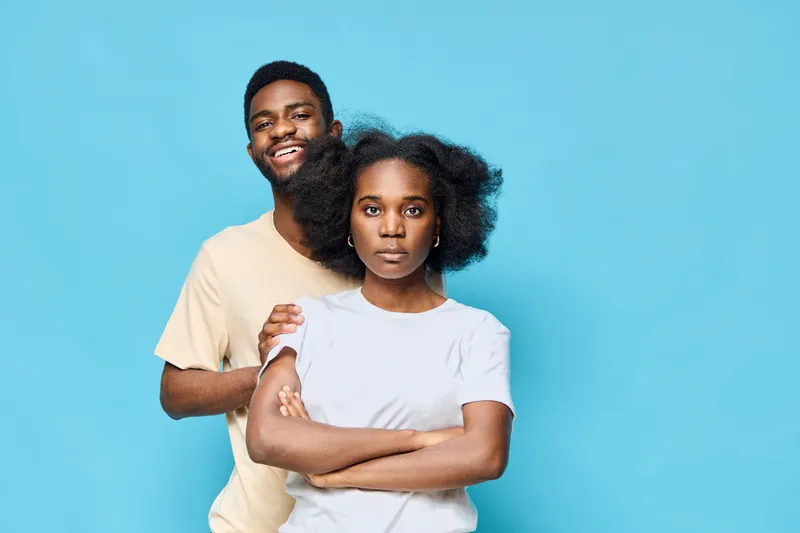 Happy young African couple with contrasting expressions standing against a blue background, showcasing emotions, clothing style, and modern vibes