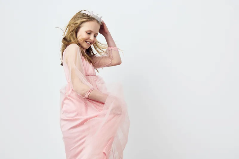 Joyful young girl in a pink dress with a floral crown, expressing happiness against a minimalistic background, ideal for childhood celebrations and happiness concepts