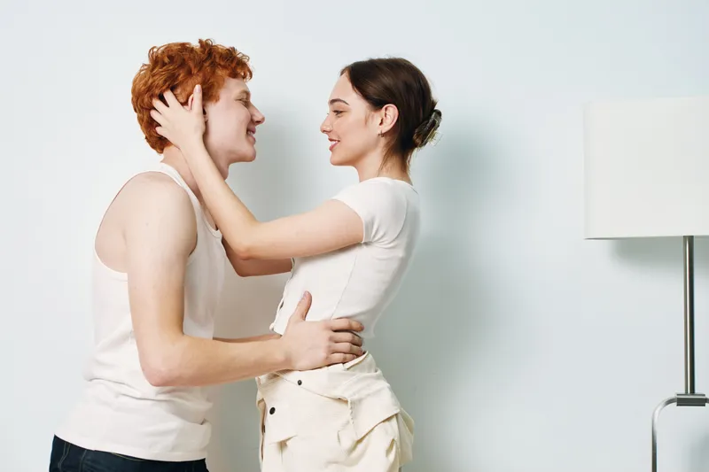 Couple, woman and man embracing indoors with smiles, holding each other gently in casual clothing. Young people showing affection, happiness and connection at home in bright room.