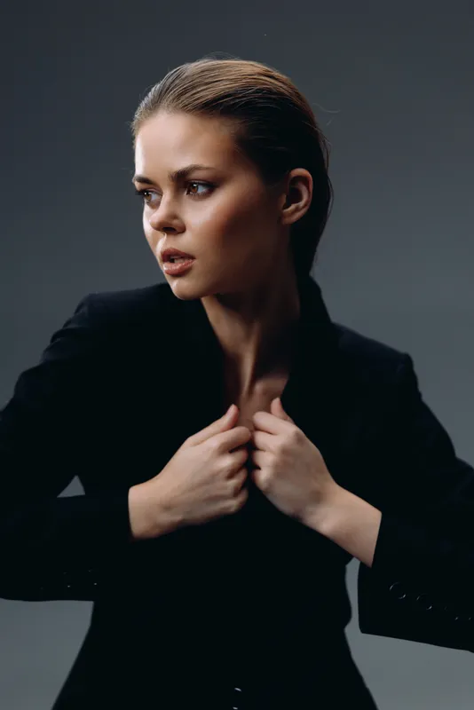 Serious woman in black suit looking away with dark moody background and confident expression.